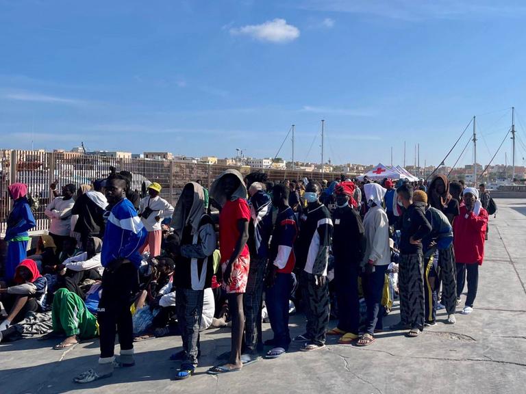 Migranten erreichen die Insel Lampedusa und warten in einer Schlange.