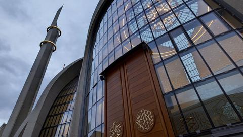 Blick auf die Zentralmoschee in Köln. In der Mitte des Bildes ist die Eingangstür zu sehen, rechts danebem blickt die Kamera in das Innere der Zentralmoschee in Köln-Ehrenfeld. Die oben gläserne Kuppel ist zu sehen. 