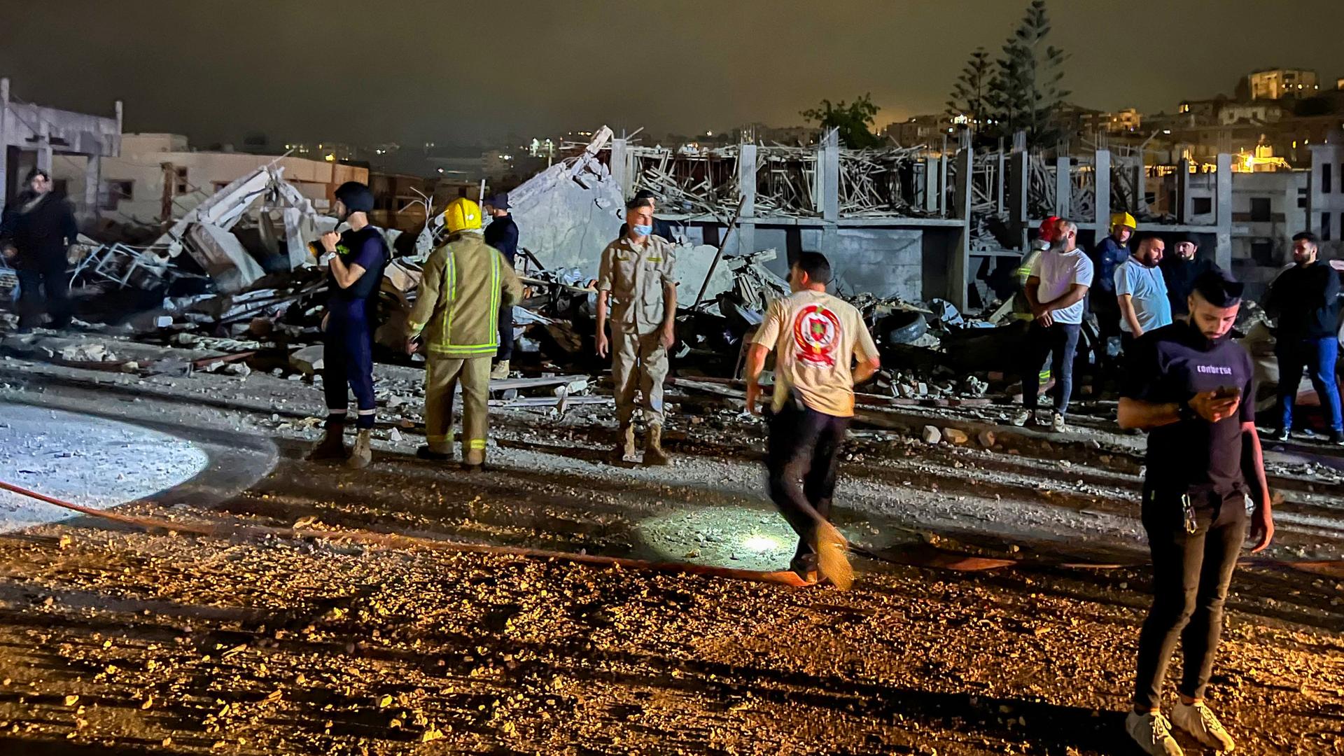 Feuerwehrleute und zivile Helfer stehen nachts vor Haustrümmern. 