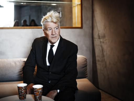 David Lynch sitzt 2017 bei einem Pressetermin auf einem Sofa und schaut nach rechts.