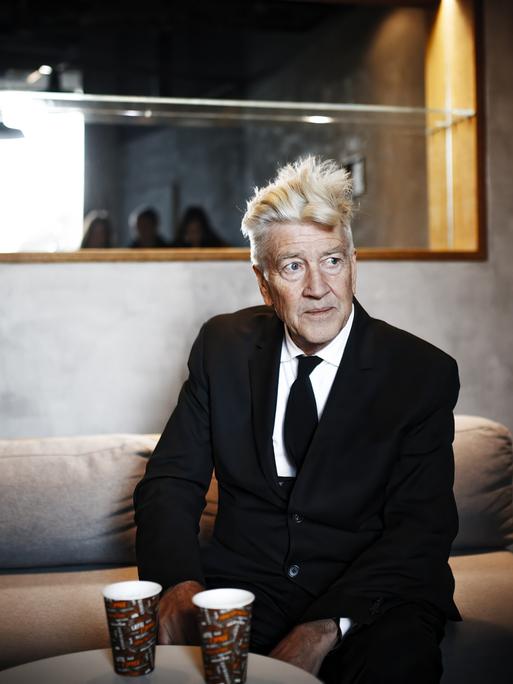 David Lynch sitzt 2017 bei einem Pressetermin auf einem Sofa und schaut nach rechts.