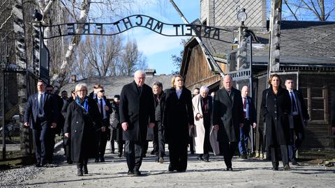 Polen, Oswiecim: Bundespräsident Steinmeier (4.v.r.) und seine Frau Elke Büdenbender (3.v.r.) gehen zusammen mit Bundeskanzler Scholz (2.v.r., SPD) und seiner Frau Britta Ernst (r) durch das Tor des ehemaligen deutschen Konzentrations- und Vernichtungslager Auschwitz-Birkenau, Stammlager Auschwitz I, mit dem Schriftzug "Arbeit macht frei".