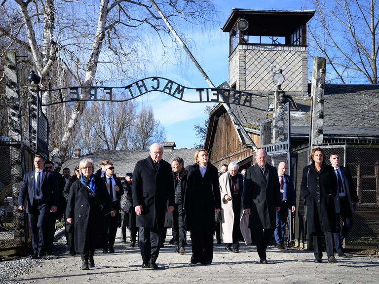 Polen, Oswiecim: Bundespräsident Steinmeier (4.v.r.) und seine Frau Elke Büdenbender (3.v.r.)  gehen zusammen mit Bundeskanzler Scholz (2.v.r., SPD) und seiner Frau Britta Ernst (r) durch das Tor des ehemaligen deutschen Konzentrations- und Vernichtungslager Auschwitz-Birkenau, Stammlager Auschwitz I, mit dem Schriftzug "Arbeit macht frei".