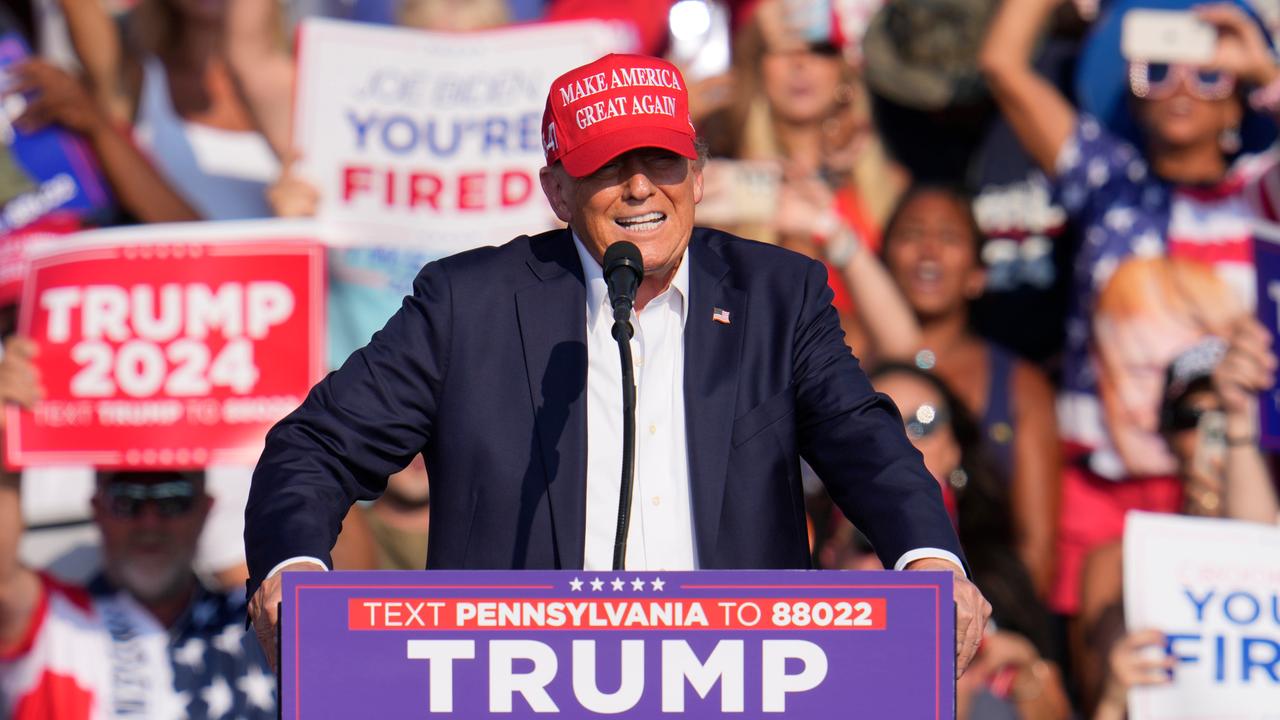 Donald Trump steht hinter einem Rednerpult mit seinem Namen und trägt eine rota "Make America Great Again"-Kappe.