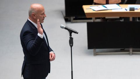 Kai Wegner (CDU)  im dunklen Anzug steht vor einem Mikrofon und hebt die rechte Hand. Er ist im seitlichen Profil zu sehen.