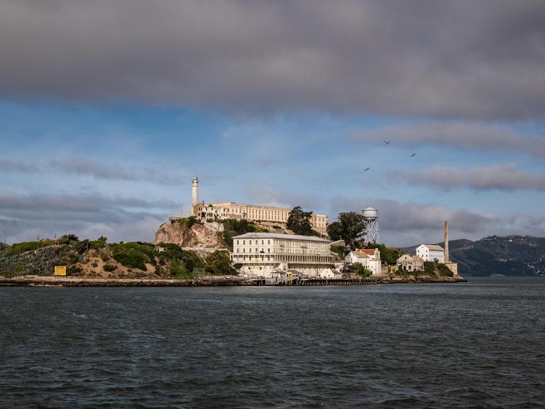 Wir sehen das Gefängnis Alcatraz, das auf einer Insel umgeben von Wasser in der Bucht von San Francisco liegt. 