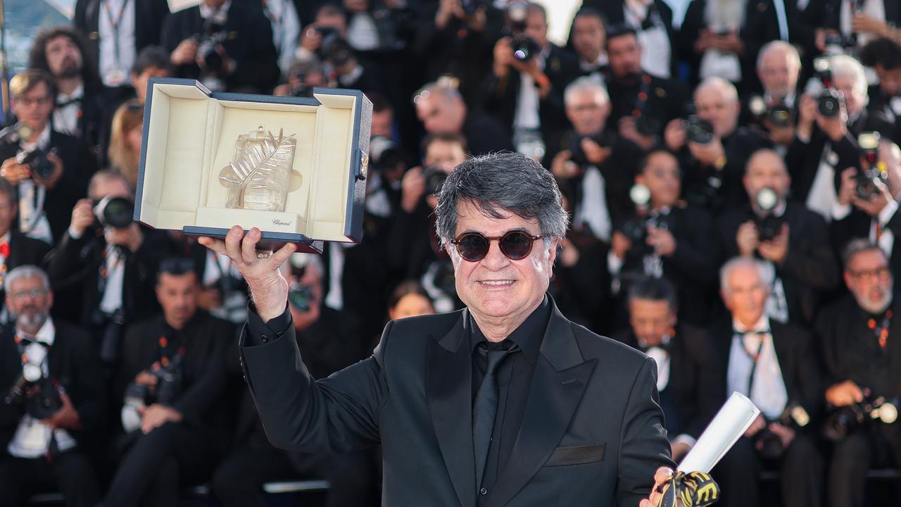 Der iranische Regisseur Jafar Panahi mit Sonnebrille hält lächelnd seine Auszeichnung nach oben und schaut in die Kamera. Dahinter viele Pressefotografen.