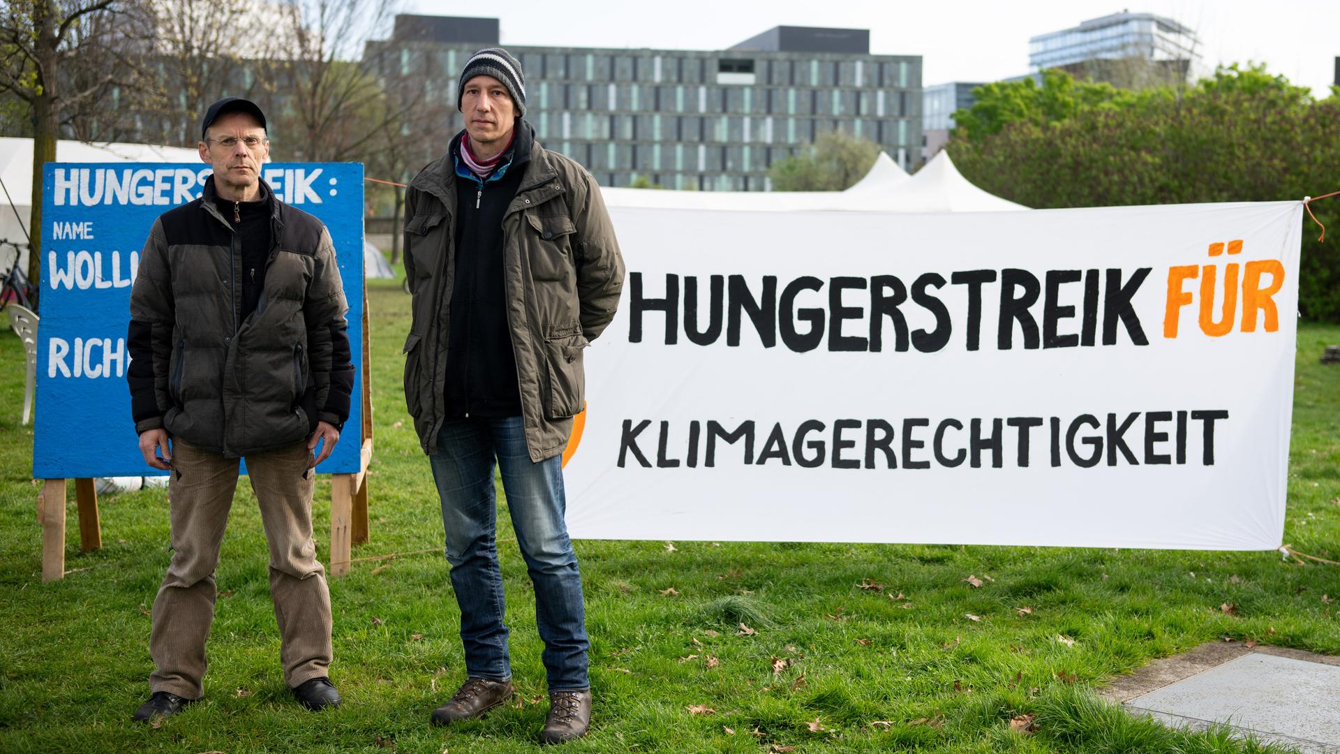 Zwei Personen stehen neben einem Banner, auf dem "Hungerstreik für Klimagerechtigkeit" steht. 
