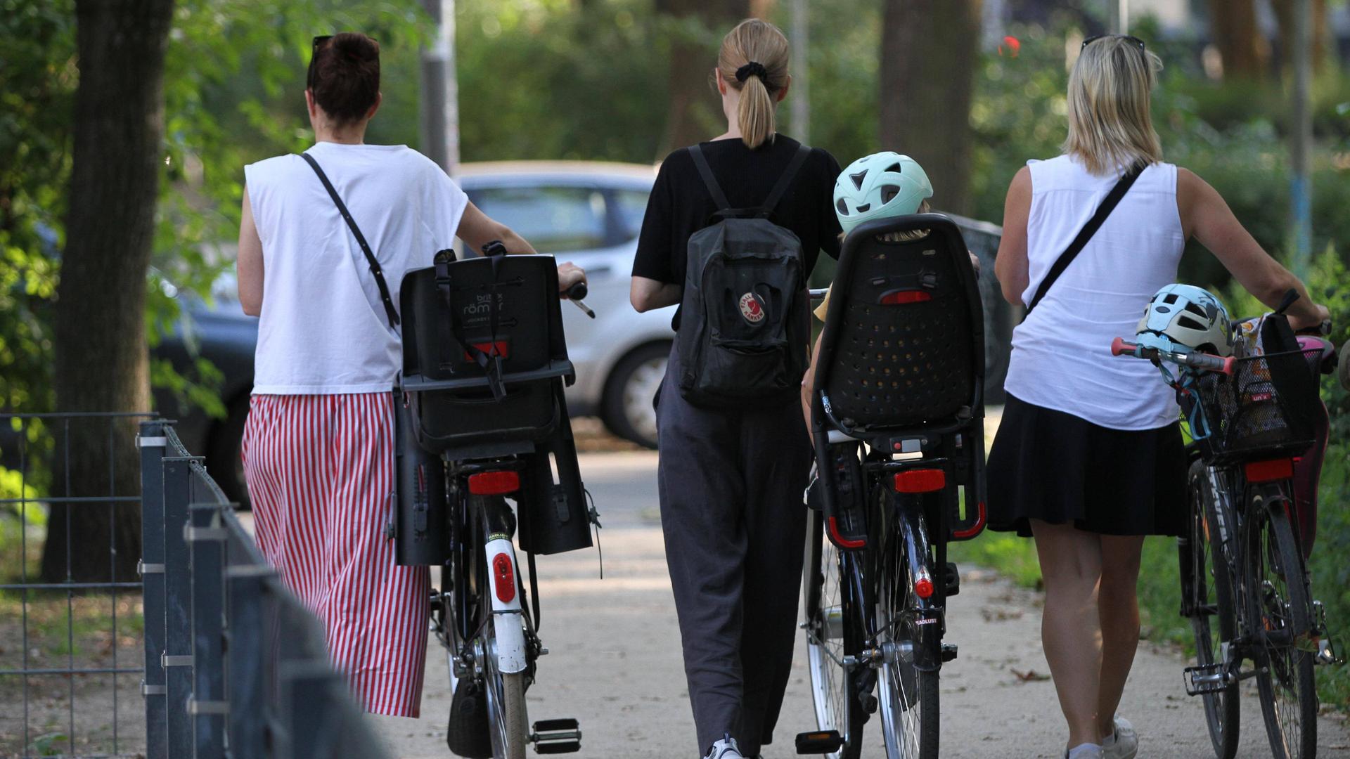 Drei Frauen mit Fahrrädern mit Kindersitzen unterwegs in einem Park.