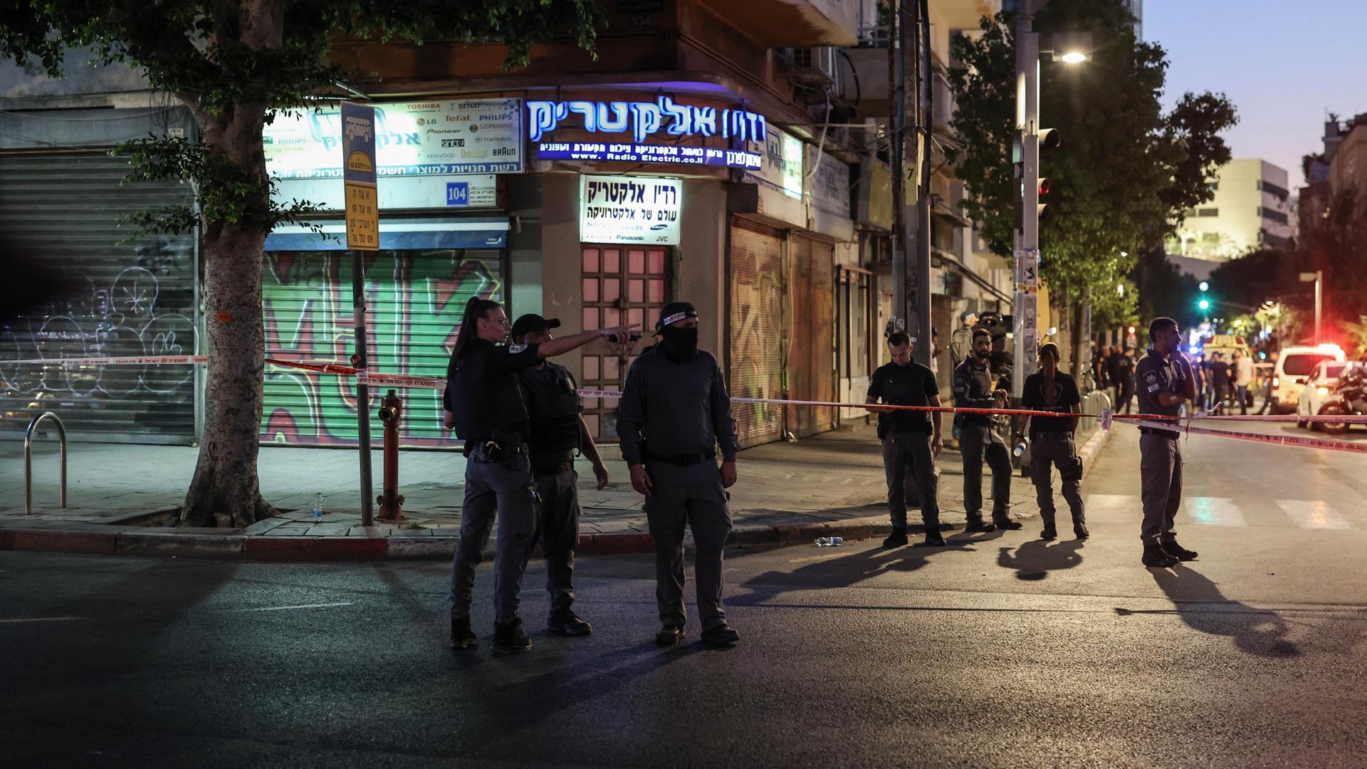 Israelische Polizisten stehen am Tatort an einer Straßenkreuzung. Absperrband ist über die Straße gezogen. Es ist dunkel. Israelische Polizisten stehen am Tatort an einer Straßenkreuzung. Absperrband ist über die Straße gezogen. Es ist dunkel.