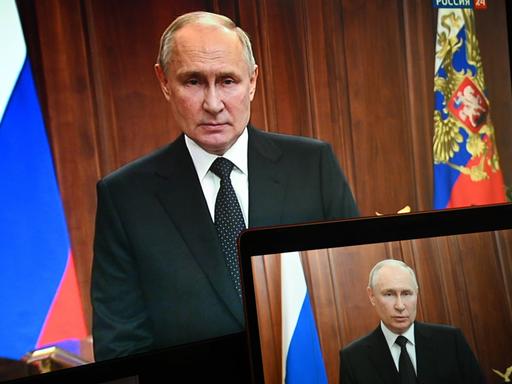 Russlands Präsident Putin neben einer Fahne und einem Monitor, auf der er auch zu sehen ist