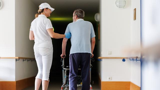 Eine ambulante Pflegefachkraft begleitet einen Bewohner des Betreuten Wohnens mit seiner Gehhilfe durch das Gebäude.