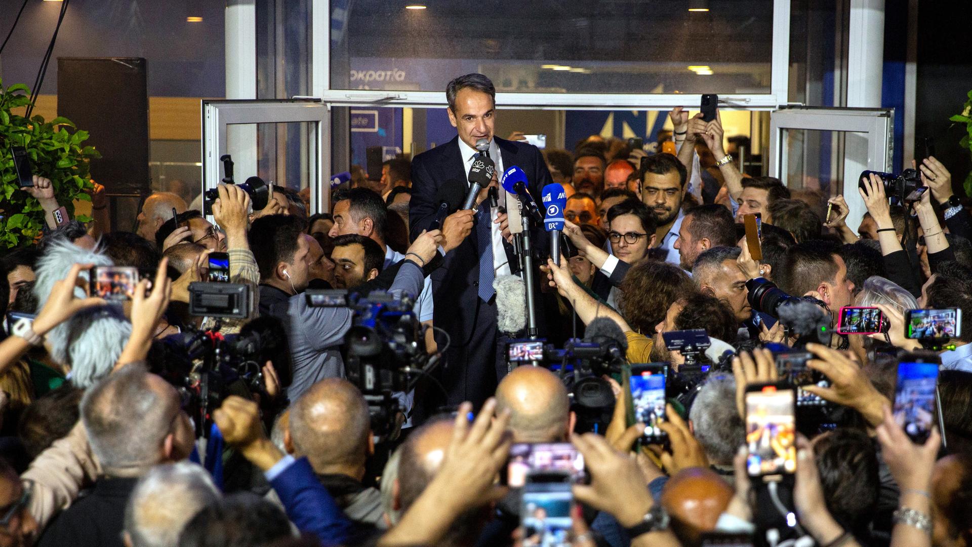 Kyriakos Mitsotakis, griechischer Ministerpräsident und Vorsitzender der Nea Dimokratia, vor der Parteizentrale in Athen. Er steht erhöht und spricht zu zahlreichen Journalisten, die Kameras und Mikrofone auf ihn richten.