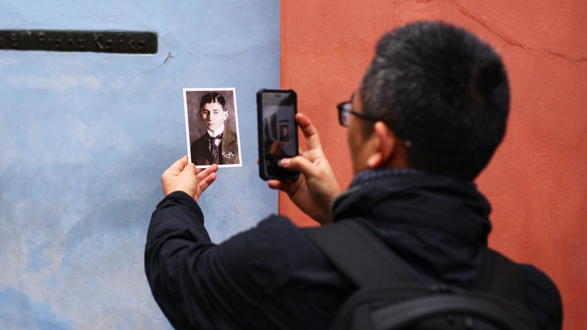 Ein asiatischer Tourist fotografiert im Goldenen Gässchen in Prag ein kleines Schwarzweißporträt Franz Kafkas vor seinem ehemaligen Haus.