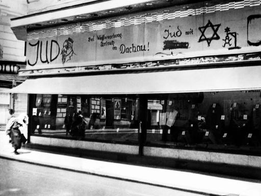 Im jüdischen Viertel in Wien, 1938. Beleidigungen und Drohungen stehen mit schwarzer Schrift über dem Schaufenster eines Geschäftes: "Bei Wegwaschung Urlaub in Dachau" und ein Männchen hängt an einem Galgen.