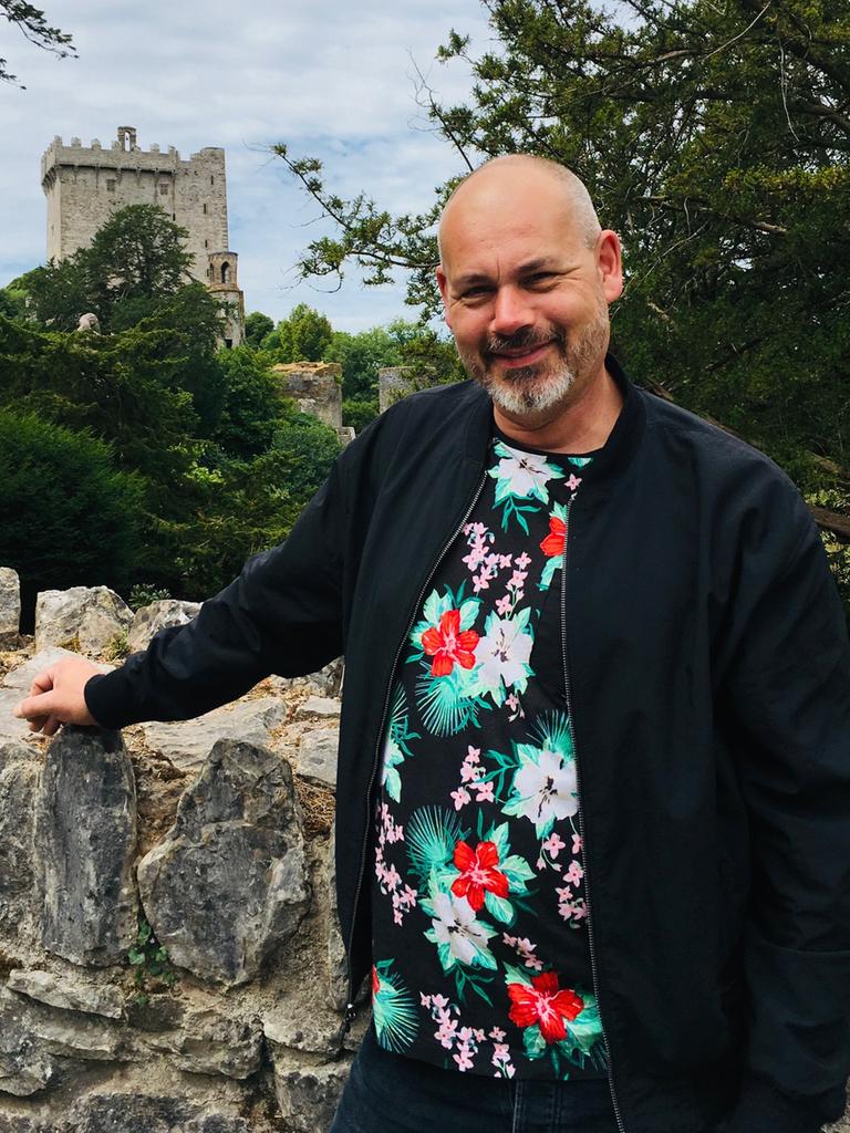 Alfons Mühlenbrock steht mit dem Arm an eine Mauer gestützt. Im Hintergrund ist der Turm einer Burg erkennbar.