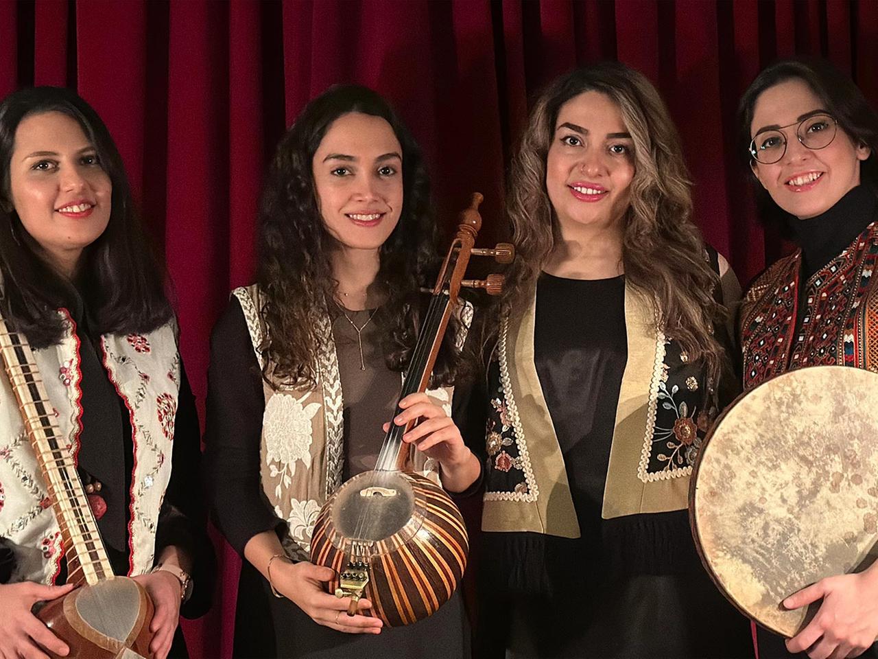 Vier Frauen stehen mit drei iranischen, traditionellen Instrumenten und lachen in die Kamera.