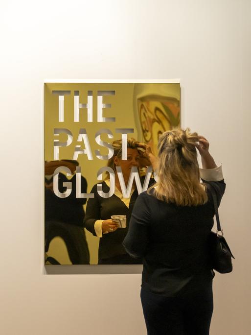 Eine Frau steht vor einem goldschimmernden Kunst auf der Art Basel 2024. (Quelle: picture alliance)
