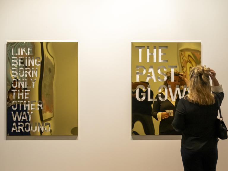 Eine Frau steht vor einem goldschimmernden Kunst auf der Art Basel 2024. (Quelle: picture alliance)
