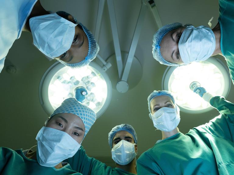 Eine Gruppe von Chirurginnen und Chirurgen schaut im Operationssaal während einer Operation auf den Patienten.