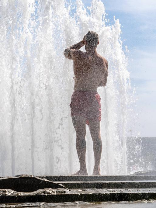 Bei Temperaturen von über 30 Grad erfrischt sich ein Mann in Badehose im Lustgarten unter der Fontäne, Berlin, 11. Juli 2023, 