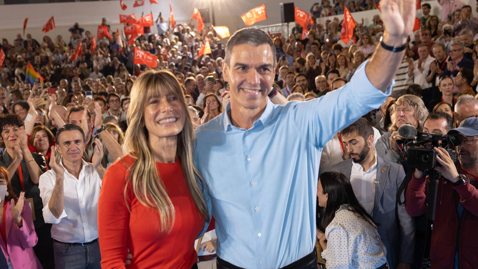 Begoña Gómez und Pedro Sánchez stehen auf einer Veranstaltung vor vielen Menschen und winken.
