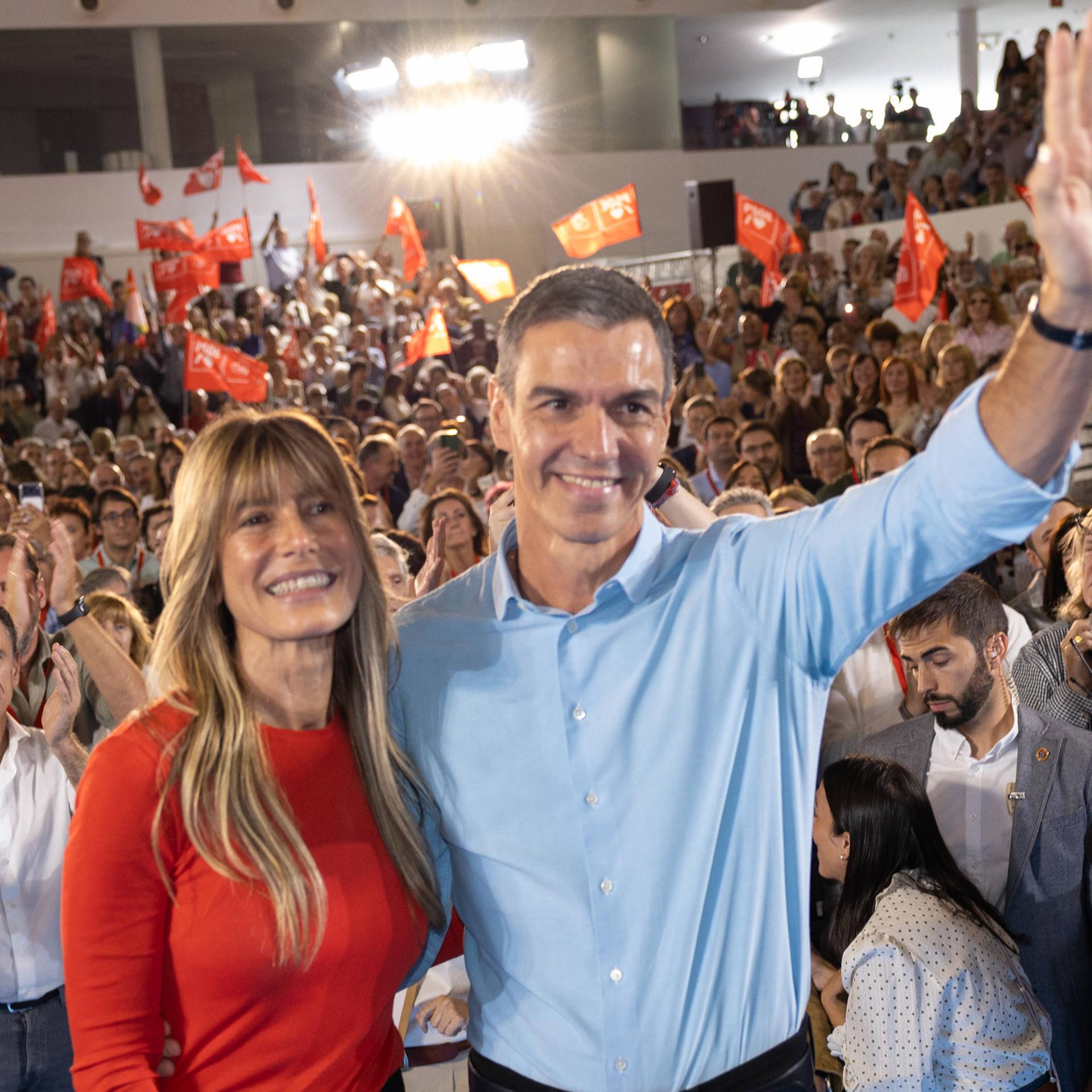 Begoña Gómez und Pedro Sánchez stehen auf einer Veranstaltung vor vielen Menschen und winken.