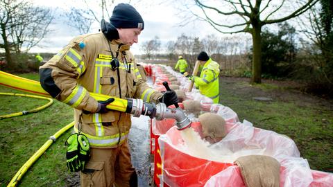 Ein Feuerwehrmann befüllt eine große rote Tonne mit Wasser.