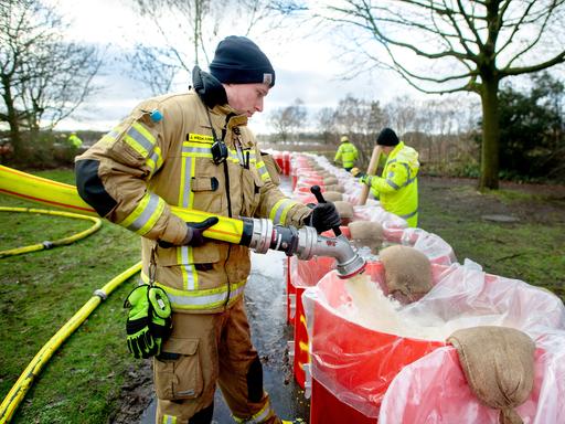Ein Feuerwehrmann befüllt eine große rote Tonne mit Wasser.