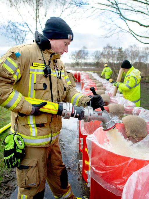 Ein Feuerwehrmann befüllt eine große rote Tonne mit Wasser.