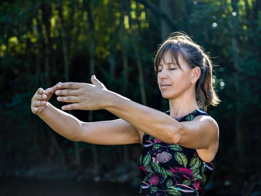 Qigong Meisterin beim üben der chinesischen Kampfkunst in der Natur. Sonnenlicht erhellt die Szene 