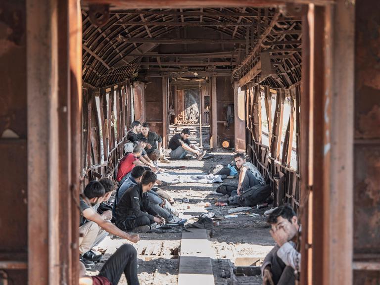 Männer sitzen in einem verrosteten Zug auf dem Boden.