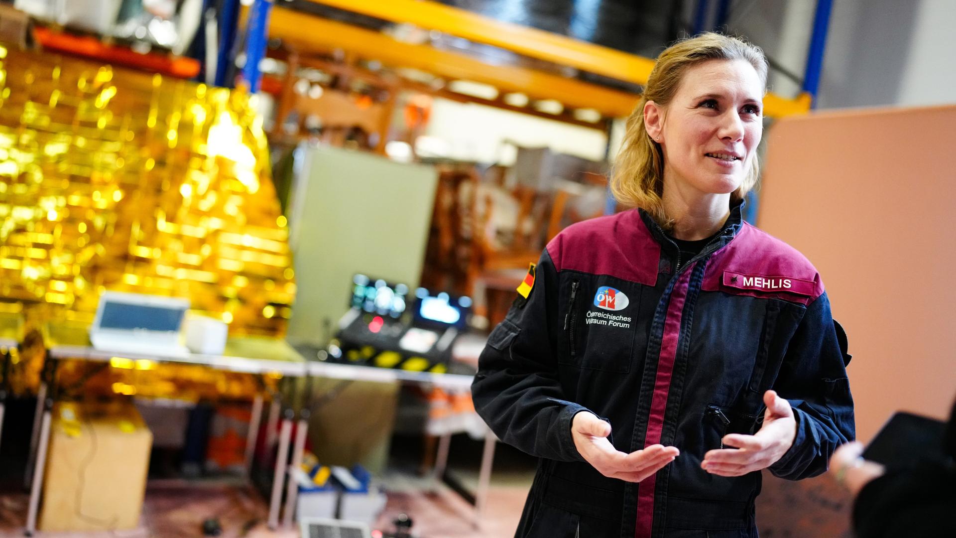 Anika Mehlis steht in einer Jacke, die ihren Namen trägt, in einem Raum und spricht gestikulierend. Anika Mehlis steht in einer Jacke, die ihren Namen trägt, in einem Raum und spricht gestikulierend.