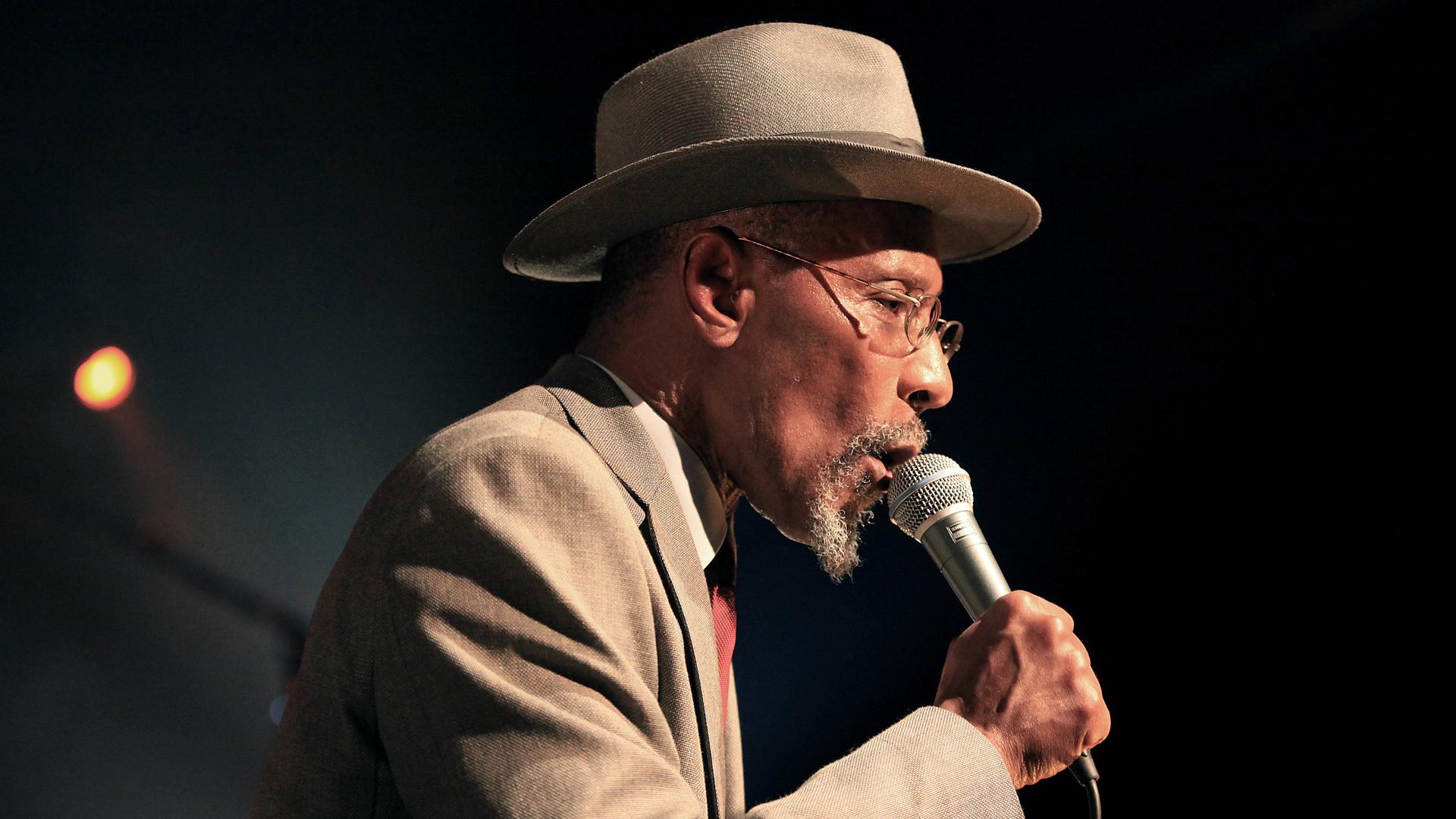 Linton Kwesi Johnson singt in ein Mikrofon.