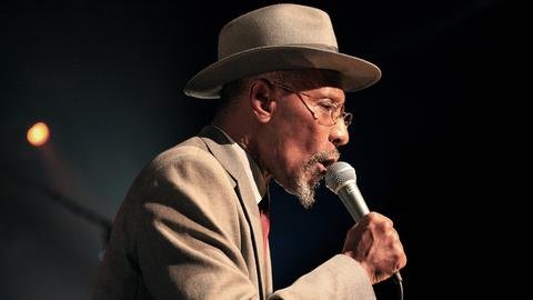 Linton Kwesi Johnson singt in ein Mikrofon.