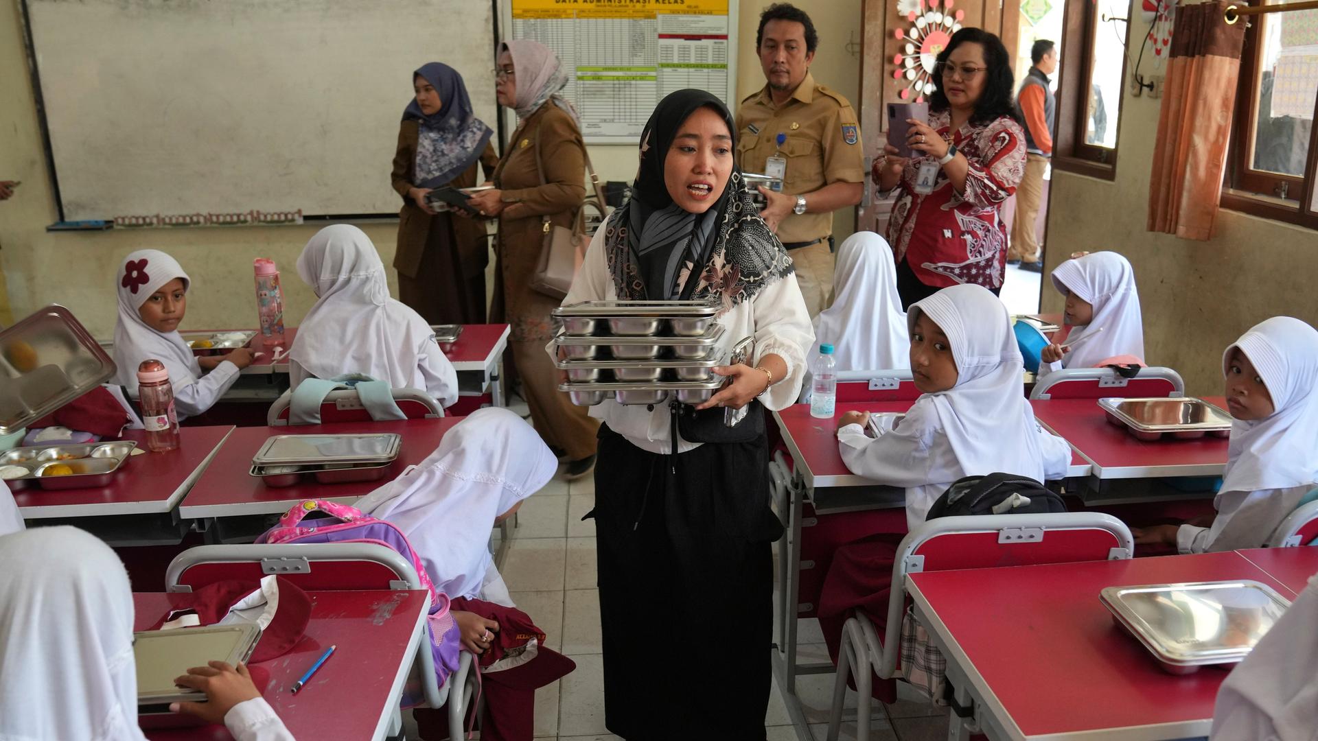 Indonesien, Depok: Ein Mitglied des Schulkomitees verteilt in einer Grundschule in Depok, West Java Mahlzeiten an Schüler.