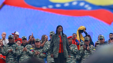 Delcy Rodriguez steht vor einer Gruppe in militärischer Kleidung. Über ihnen weht die venezolanische Flagge.  