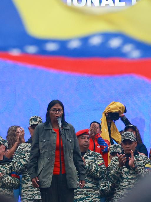Delcy Rodriguez steht vor einer Gruppe in militärischer Kleidung. Über ihnen weht die venezolanische Flagge.  