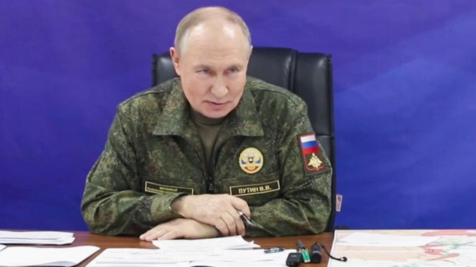 Wladimir Putin sitzt in Militäruniform an einem Tisch vor blauem Hintergrund.