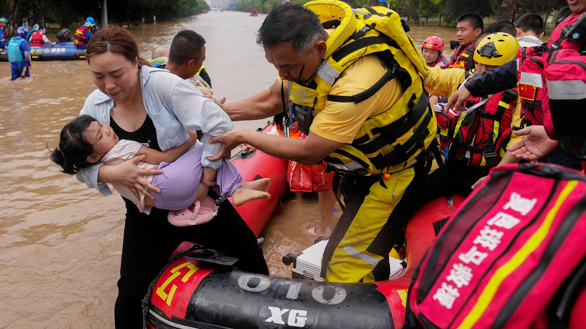 Das Foto zeigt Rettungs-Helfer in China in einem Schlauch-Boot. Die Helfer bringen gerade eine Frau und ihr Kind in Sicherheit.