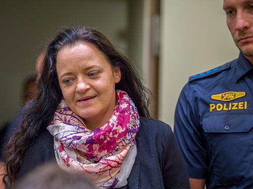 Zschäpe wird von einem Polizisten am Arm geführt, sie trägt offene schwarze Haare und einen bunten Schal. 