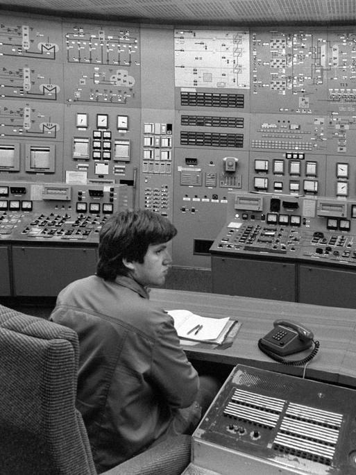 Ein Mann sitzt in einer Steuerzentrale. Diese ist im Kernkraftwerk Lubmin bei Greifswald. In dem Raum sind viel kleine Lampen und Knöpfe. Vor dem Mann steht auch ein Telefon.