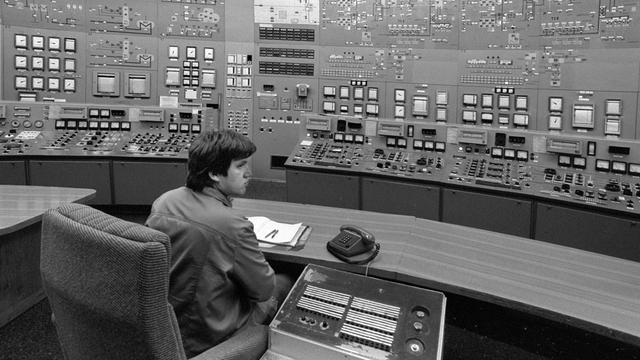 Ein Mann sitzt in einer Steuerzentrale. Diese ist im Kernkraftwerk Lubmin bei Greifswald. In dem Raum sind viel kleine Lampen und Knöpfe. Vor dem Mann steht auch ein Telefon.