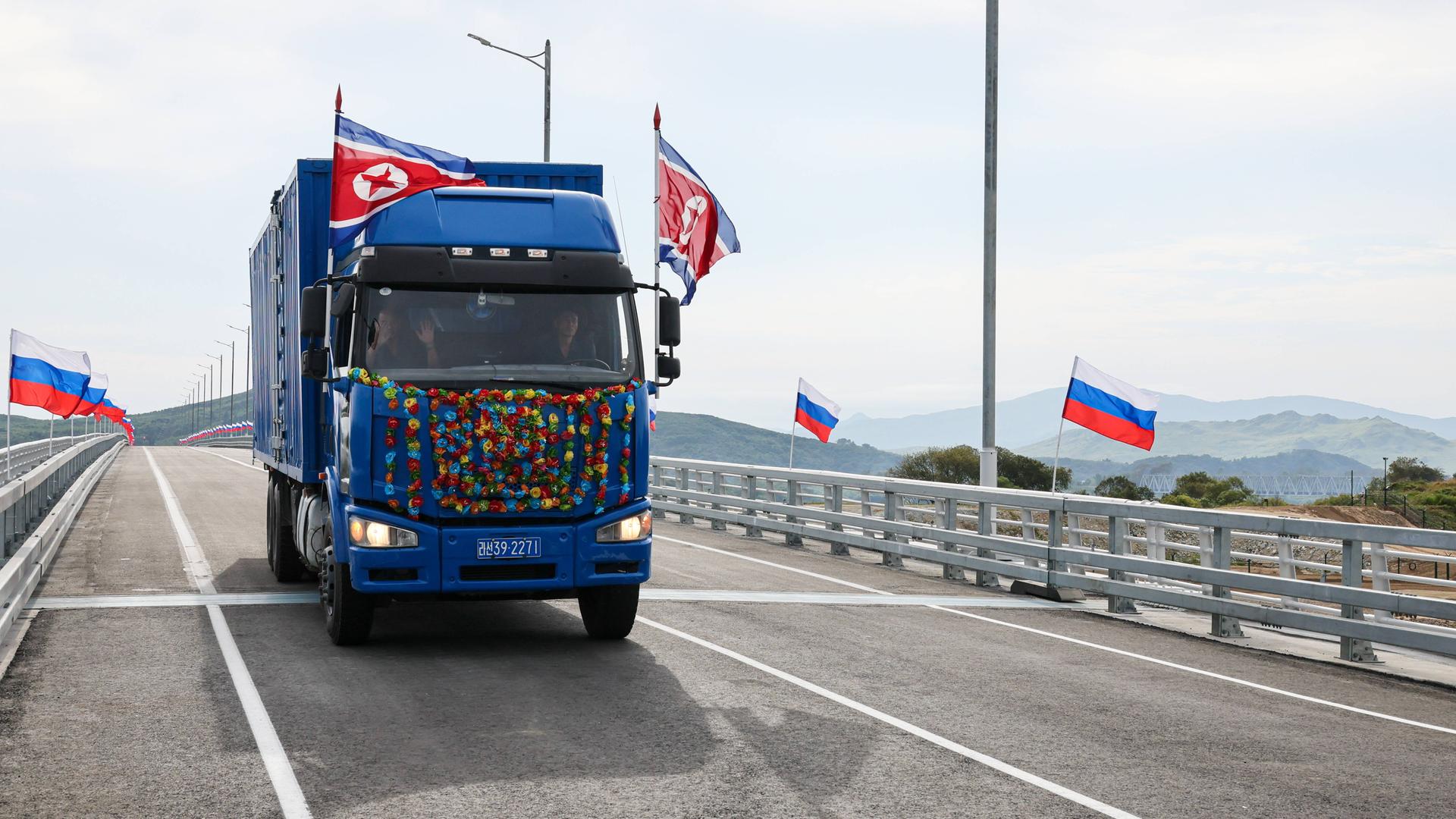 Ein Lastwagen mit nordkoreanischen Fahnen fährt über eine neue Brücke, auf der russische Fahnen wehen.