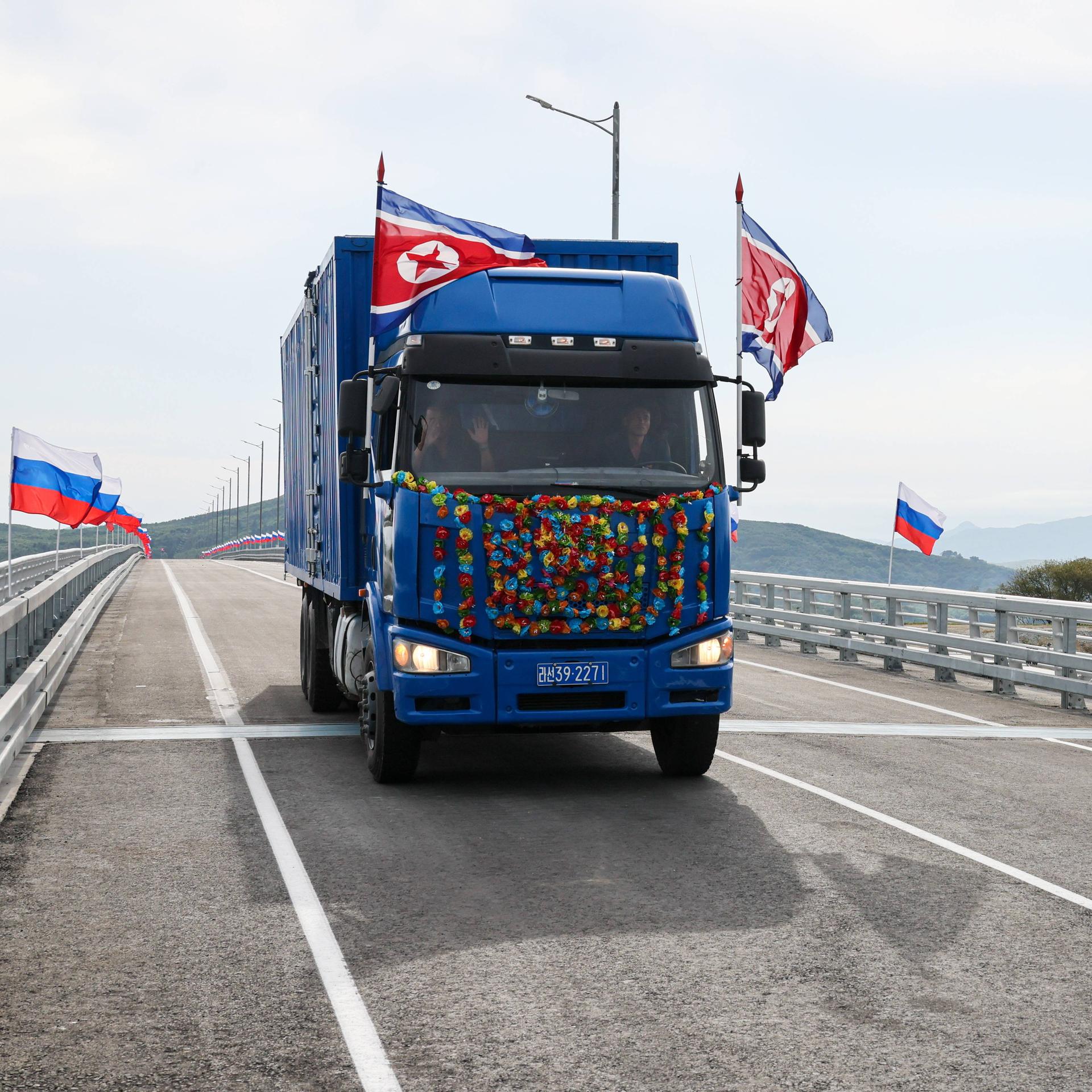 Ein Lastwagen mit nordkoreanischen Fahnen fährt über eine neue Brücke, auf der russische Fahnen wehen.