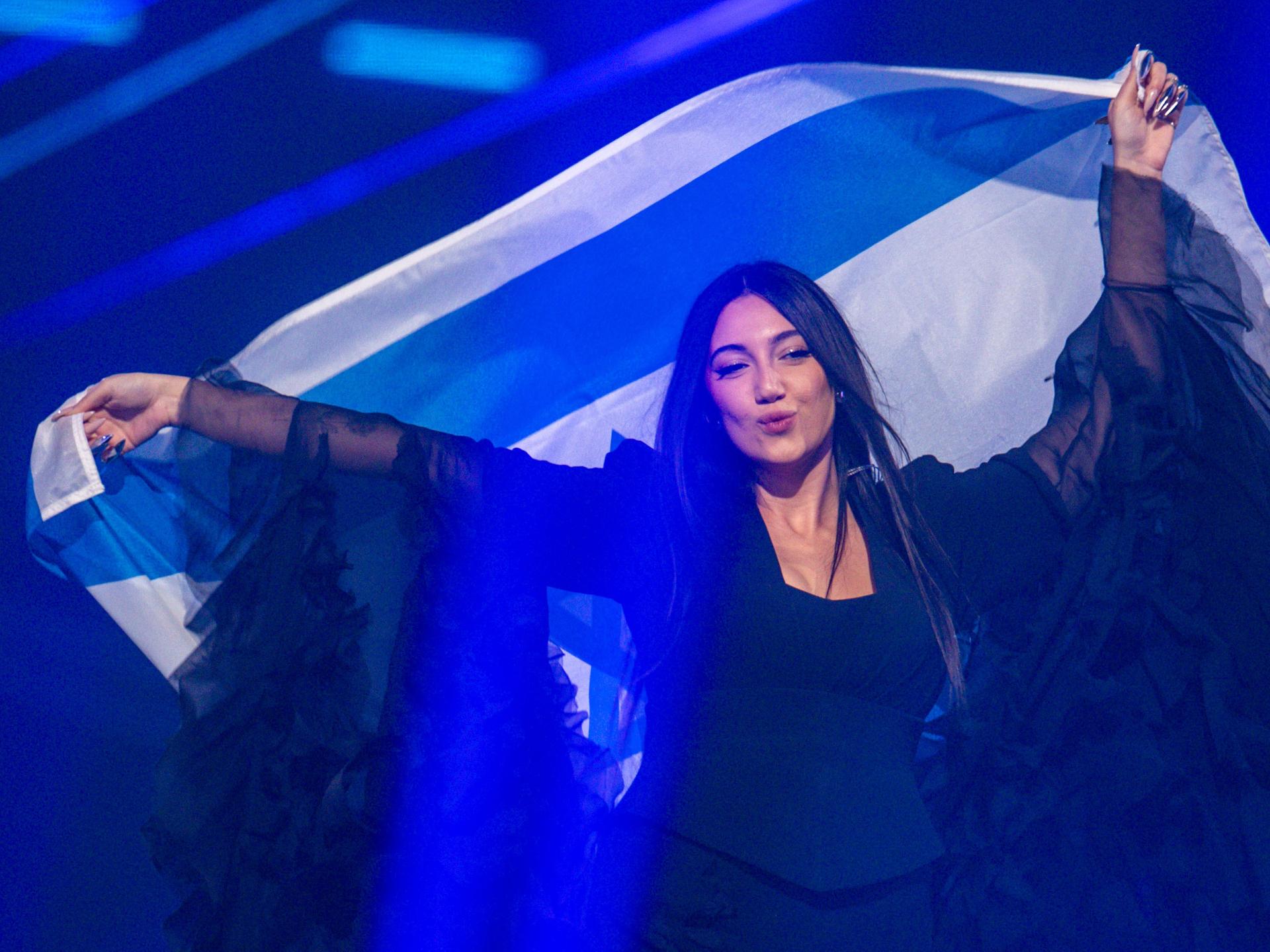 Die israelische ESC-Kandidatin Yuval Raphael steht auf einer Bühne und schwenkt eine israelische Fahne hinter ihrem Rücken.