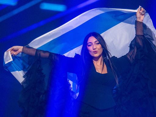 Die israelische ESC-Kandidatin Yuval Raphael steht auf einer Bühne und schwenkt eine israelische Fahne hinter ihrem Rücken.