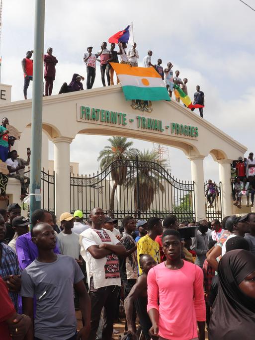 Menschen demonstrieren in Nigers Hauptstadt Niamey. Einige stehen auf einem Torbogen und schwenken Fahnen.