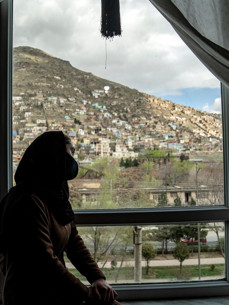 In Kabul sitzt ein junges Mädchen verschleiert an einem Fenster und blickt auf die Stadt. 