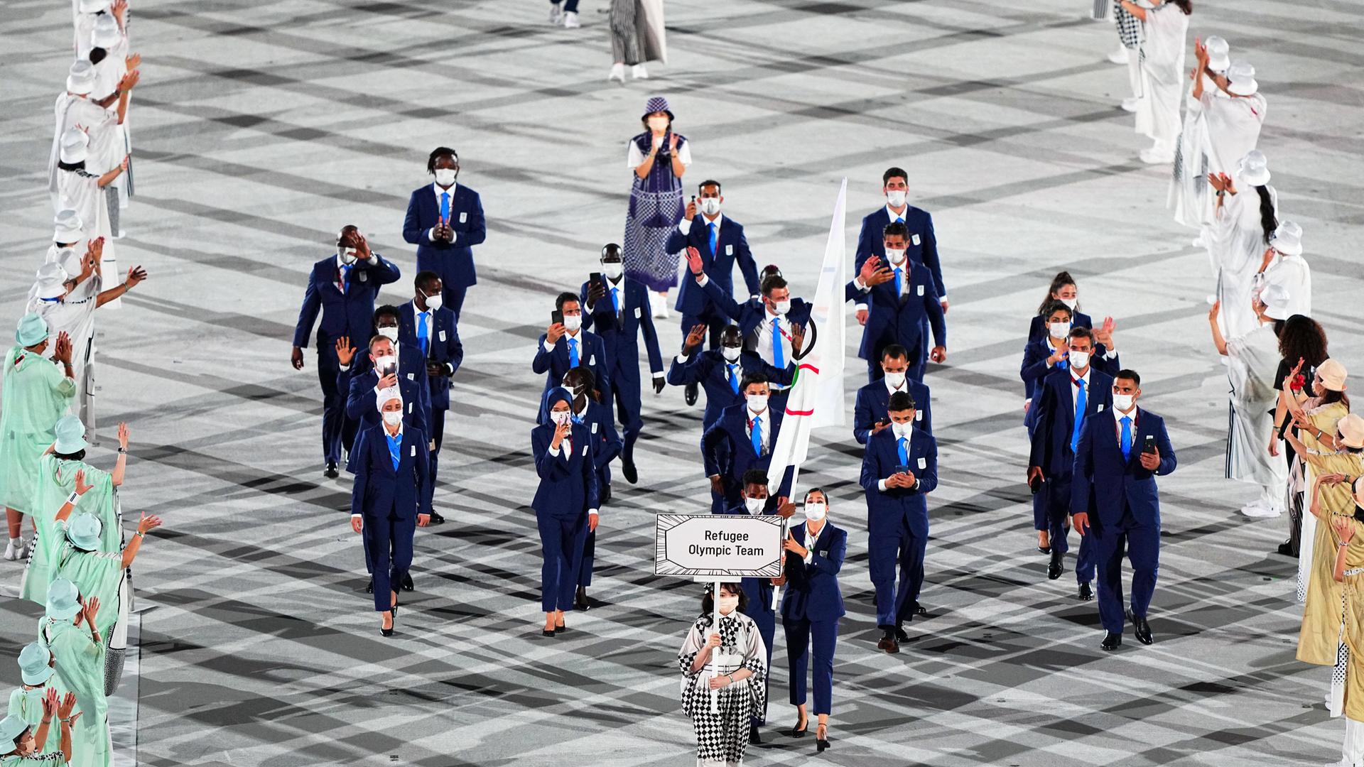 Zu sehen ist die Eröffnungsfeier bei den Olympischen Spielen in Tokio 2021, als gerade das damalige Refugee Olympic Team einläuft und dabei die Olympische Fahne hochhält.
